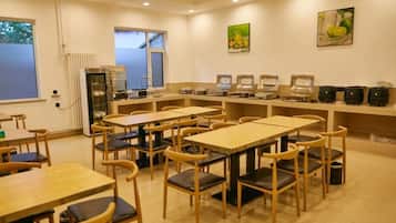A dining area with multiple tables and chairs, a kitchen area with appliances, and artwork on the walls.