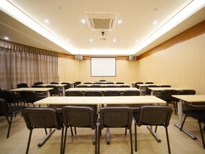 Un salón de conferencias con varias mesas y sillas, una pantalla de proyector y un equipo de aire acondicionado instalado en el techo.