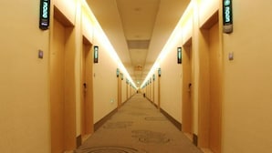 A hotel hallway with carpeted floors, wooden doors, and illuminated signs indicating room numbers. - Greentree Inn Shanghaibaoshan District Tieshan Road Youyi Road Hotel (Shanghai)