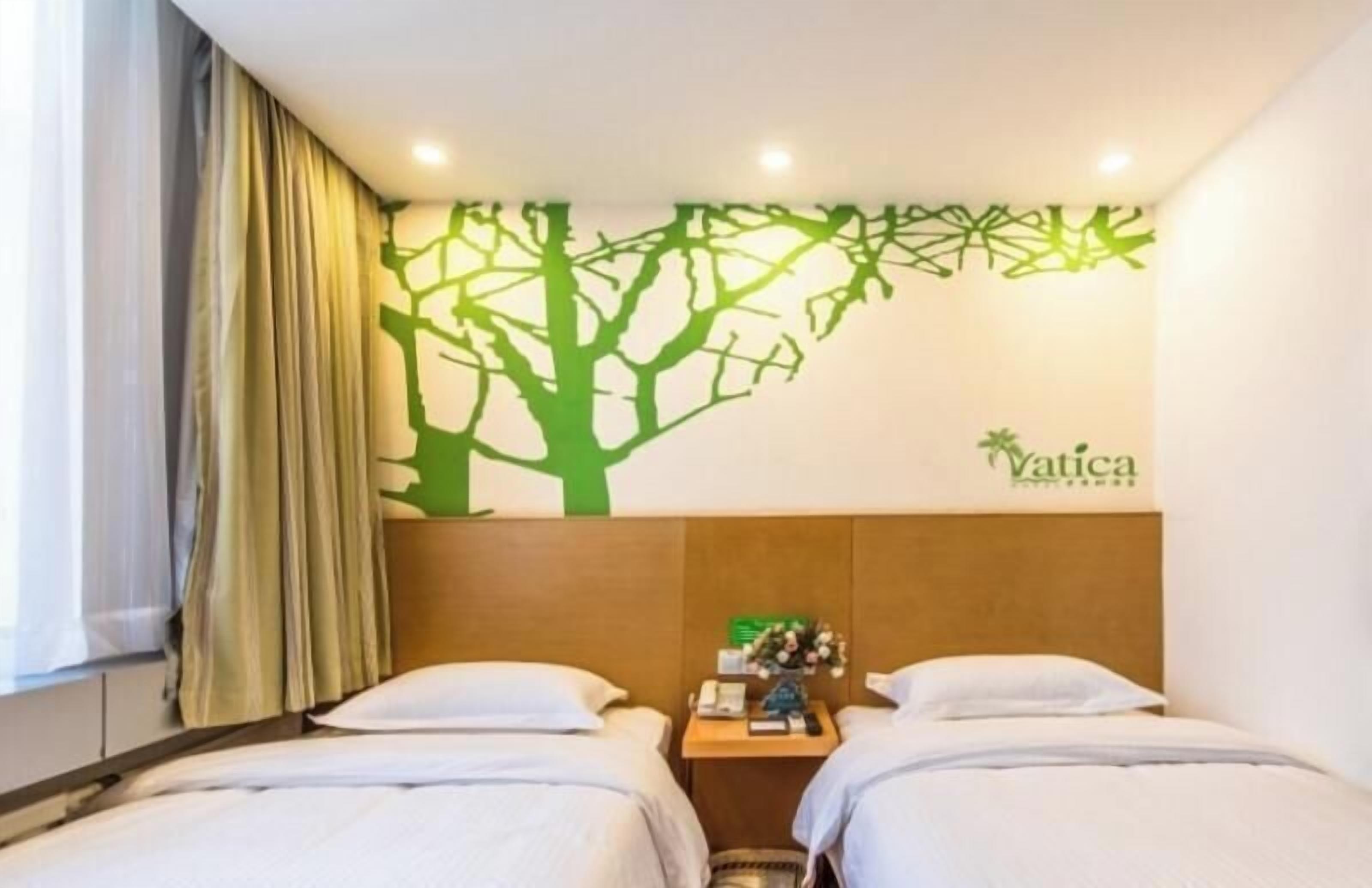 Habitación de hotel con dos camas, cabecera con un adhesivo en la pared, mesita de noche y ventana con cortinas.