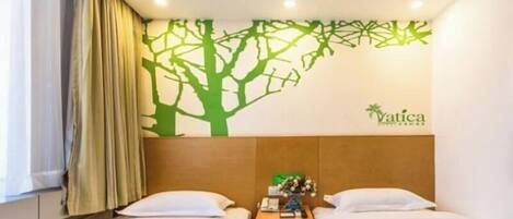 Habitación de hotel con dos camas, cabecera con un adhesivo en la pared, mesita de noche y ventana con cortinas.