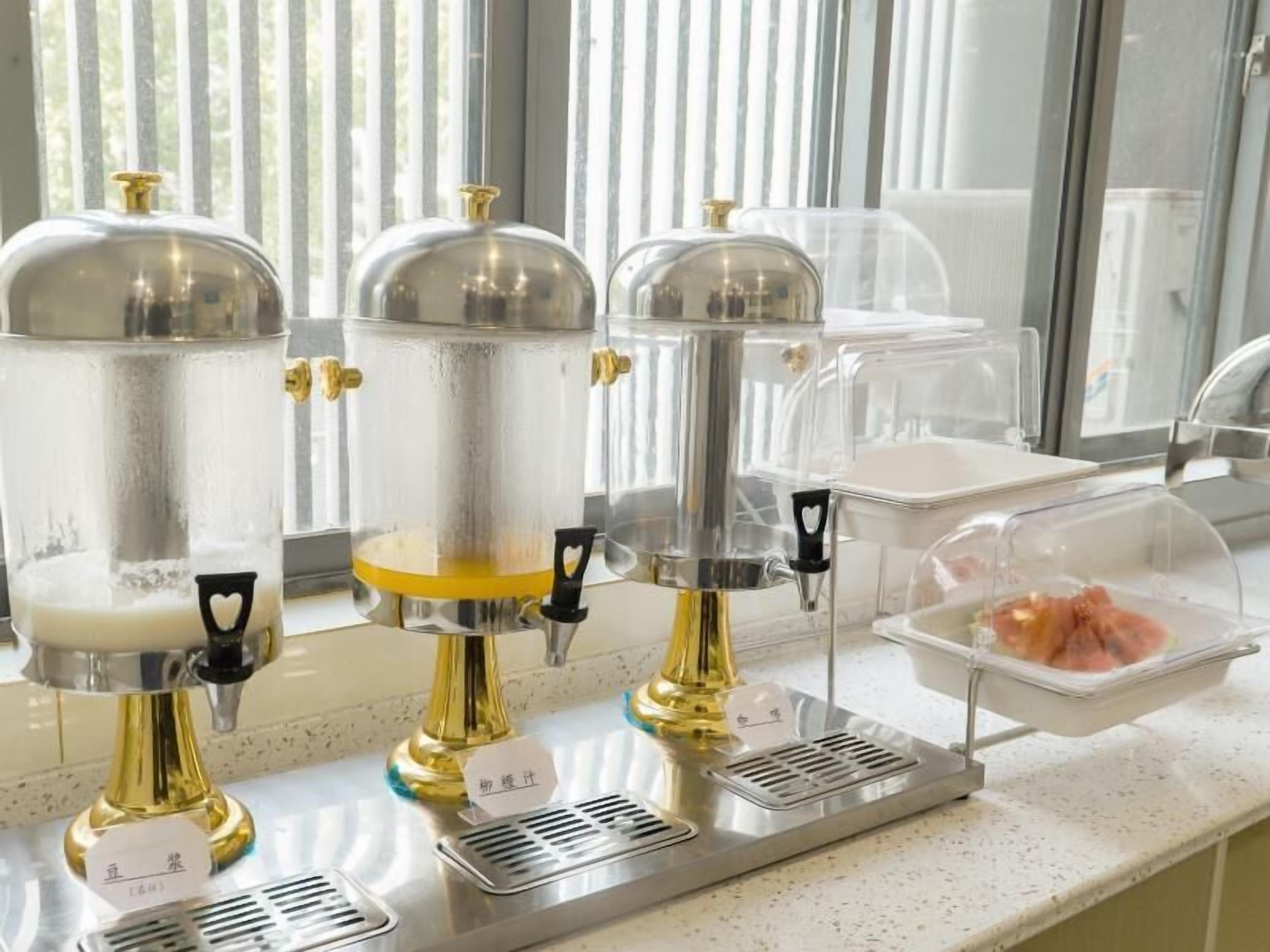 A kitchen area with three stainless steel beverage dispensers, a sink, and a countertop with a food container.