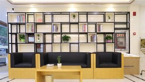 A modern library with a black leather sofa, a wooden table, and a bookshelf filled with books and plants. - Greentree Inn Yangzhou Dongguan Street Geyuan Garden Express Hotel (Yangzhou)