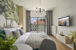 A modern hotel room with a large bed, a TV, a balcony with a city view, and a mural of trees.