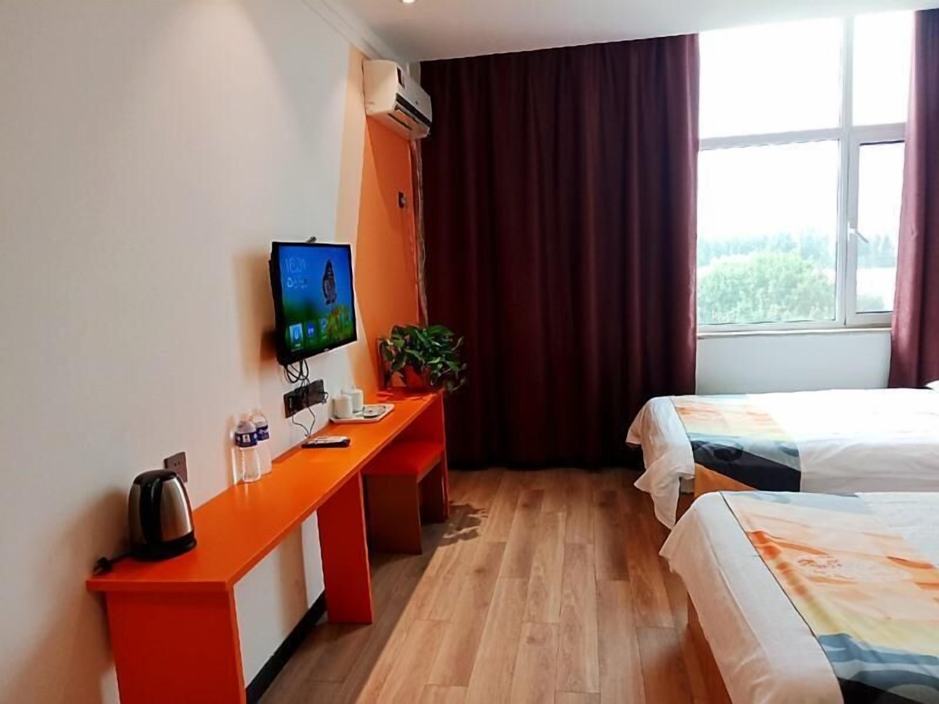 Habitación de hotel con piso de madera, un escritorio con hervidor, televisión y dos camas.