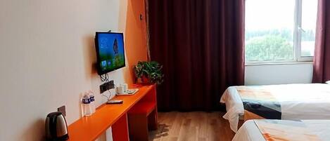 Habitación de hotel con piso de madera, un escritorio con hervidor, televisión y dos camas.