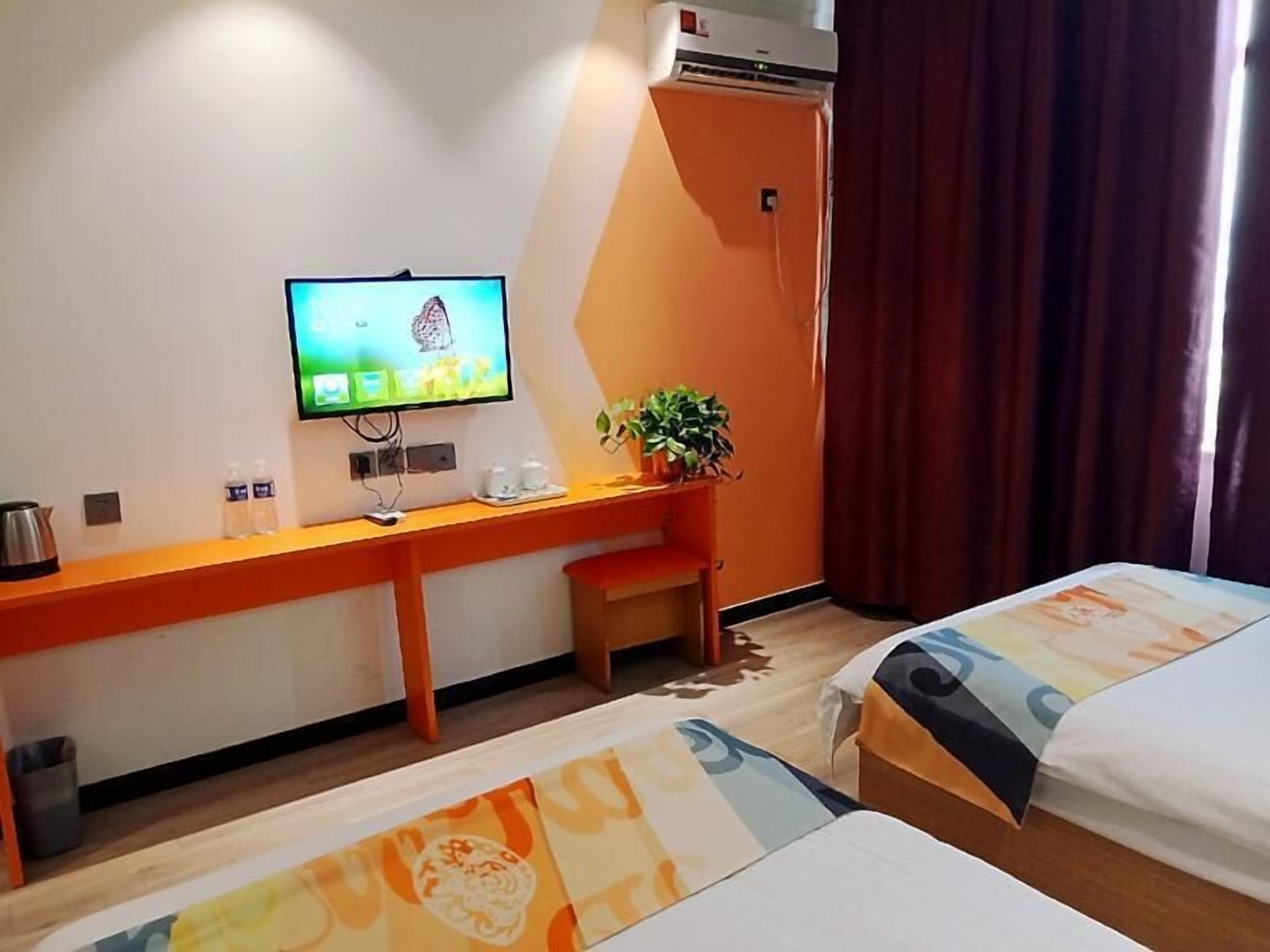 A hotel room with a bed, a desk with a television, a small table, and a potted plant.