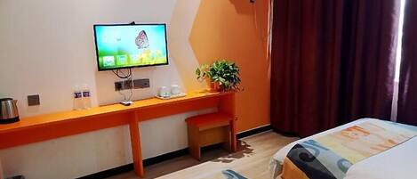 A hotel room with a bed, a desk with a television, a small table, and a potted plant.