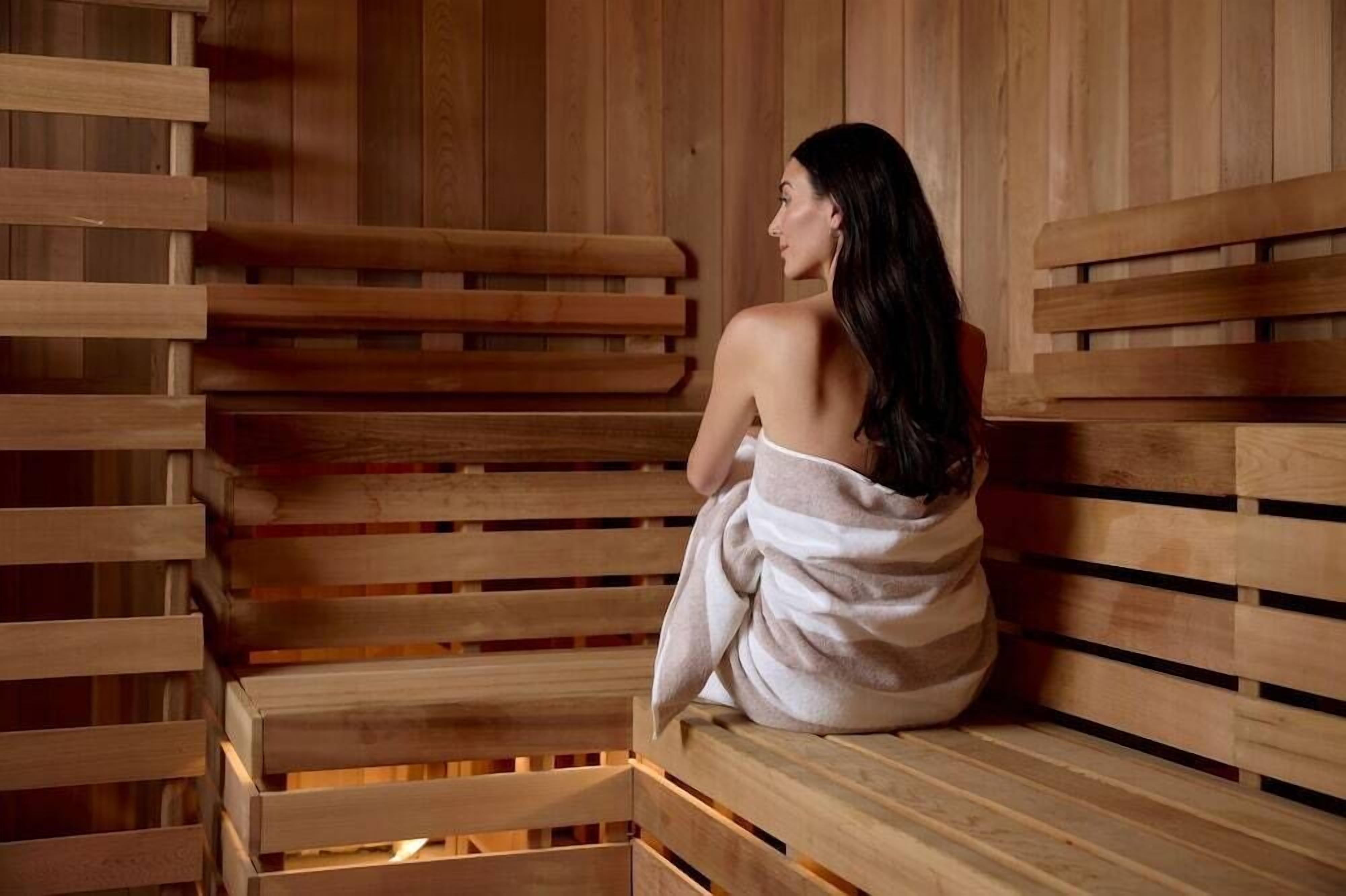 A person sitting on a wooden bench in a sauna room with wooden walls.