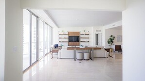 A modern living room with a large window, a central table, and a TV mounted on the wall. - Amrit Ocean Resort & Residences - Singer Island (Singer Island)