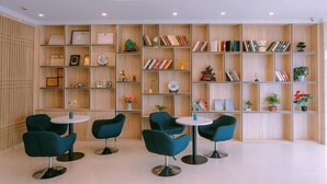 A modern library with bookshelves, decorative items, and four teal chairs around a central table. - Greentree Inn Maanshan West Jiuhua Road Wanda Plaza Mengniu Diary Express Hotel (Ma'anshan)