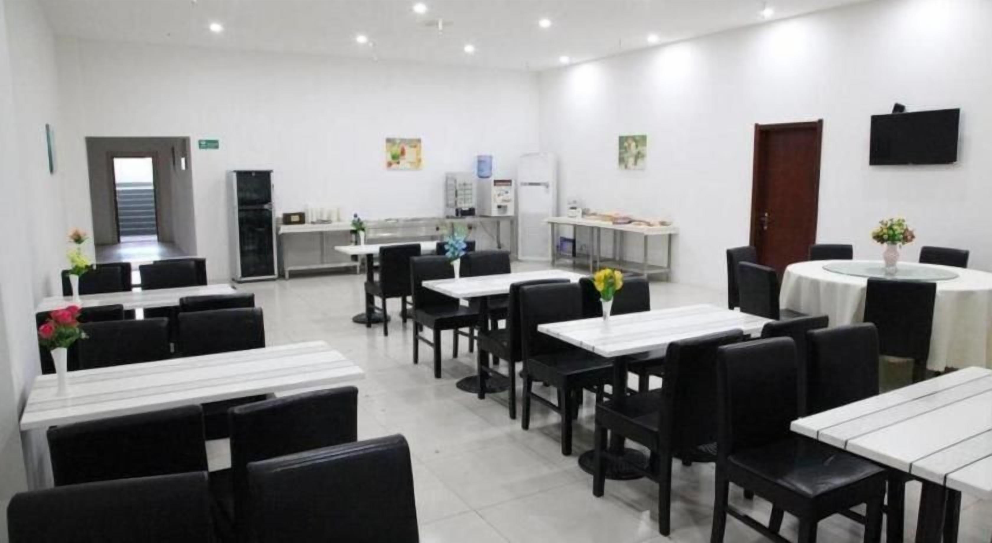 Un comedor con mesas y sillas, una cocina al fondo y una puerta que da a otra habitación.