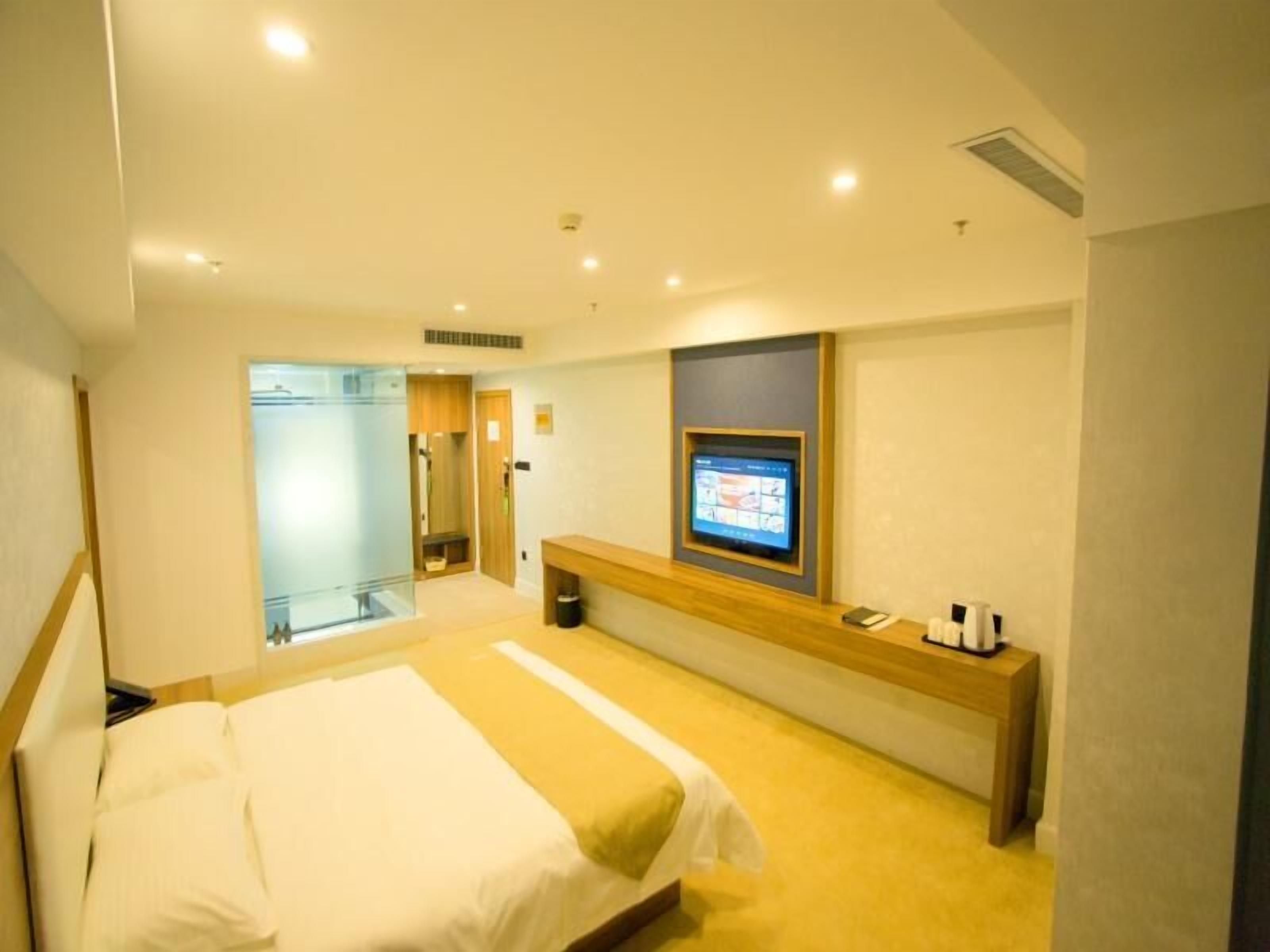 A hotel room with a bed, a TV mounted on the wall, and a small table with toiletries.