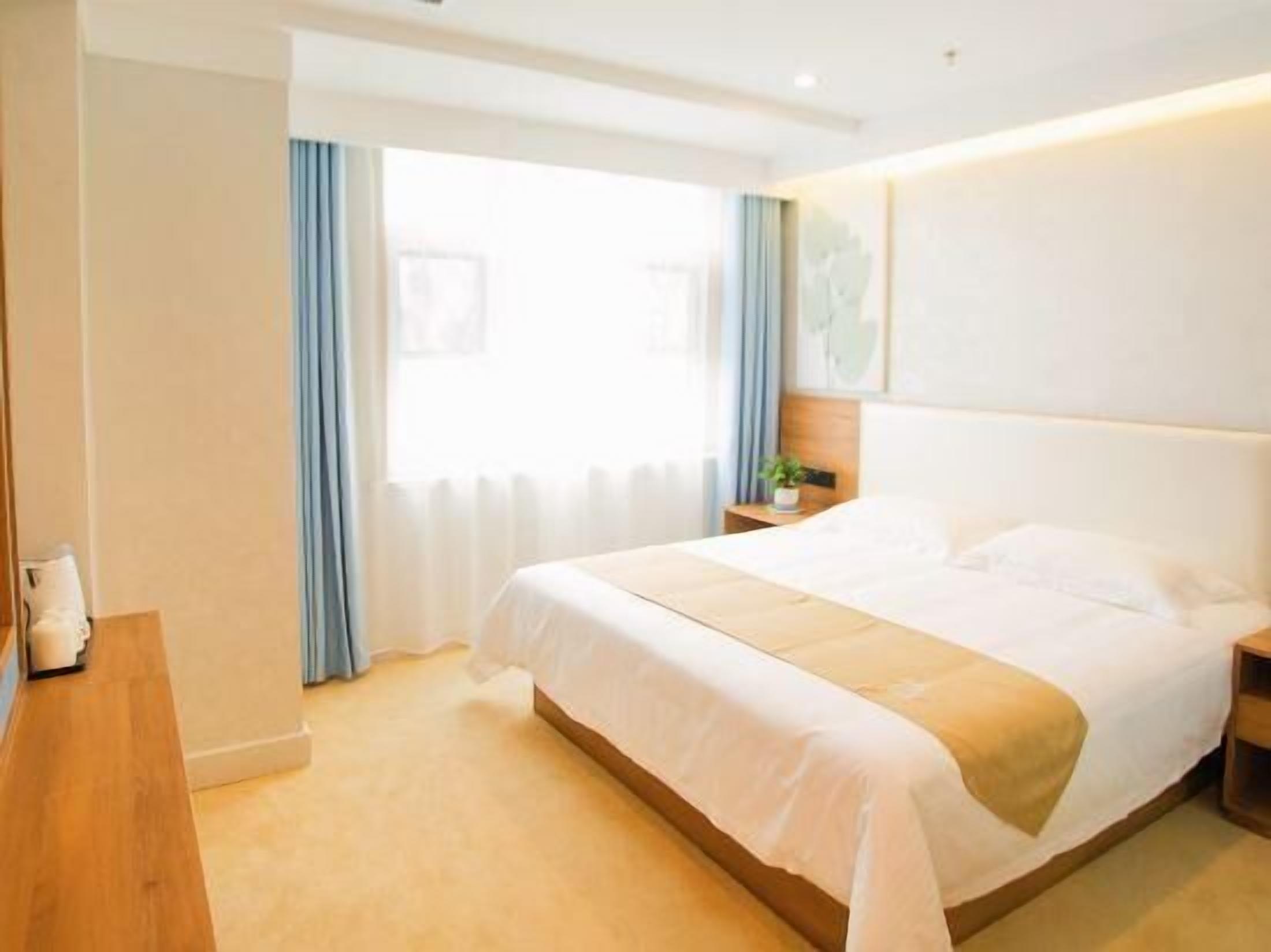 Ein Hotelzimmer mit einem großen Bett, einem Nachttisch, einem Fenster mit Vorhängen und einem Wandbild.