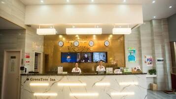 A reception desk at GreenTree Inn with a marble countertop, two receptionists, a digital screen, and a clock.