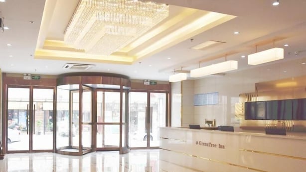 A spacious lobby with a modern design, featuring a reception desk, a revolving door, and a large chandelier. - Greentree Inn Wuxi Huishan District Yangshan Town Jiayang Life Plaza Business Hotel (Wuxi)