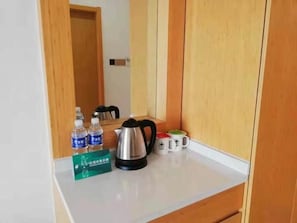 A hotel room with a wooden cabinet, a white countertop, a kettle, two water bottles, and a mug. - Greentree Inn Wuxi Huishan District Yangshan Town Jiayang Life Plaza Business Hotel (Wuxi)