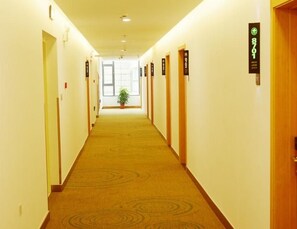 Ein Hotelgang mit Teppichboden, rechts und links Türen sowie einer Zimmerpflanze in der Mitte.