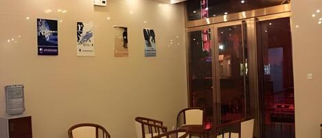 A hotel lobby with wooden chairs and tables, a glass door entrance, and wall-mounted posters.