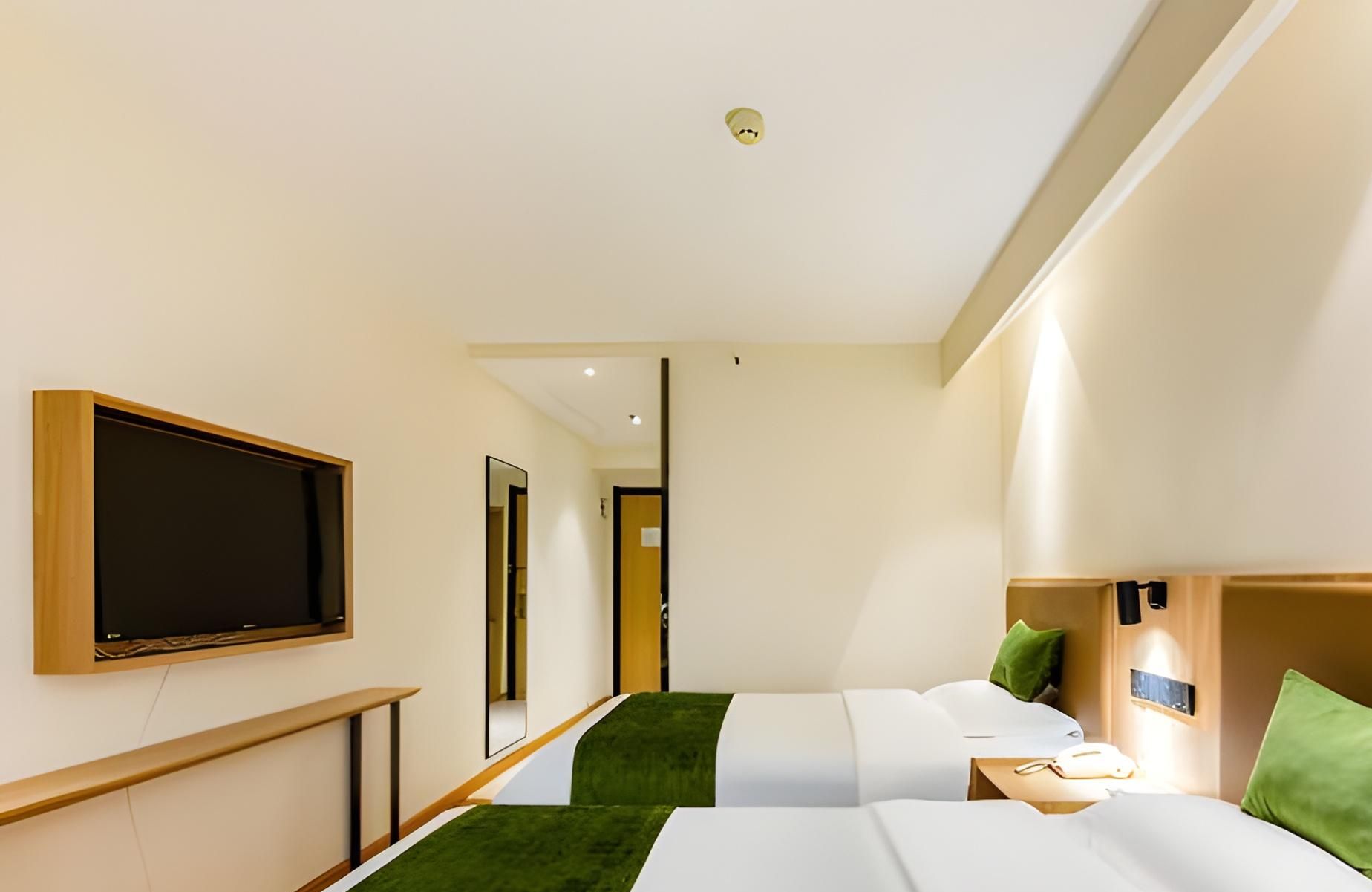 A hotel room with two beds, a TV mounted on the wall, and a green carpet.