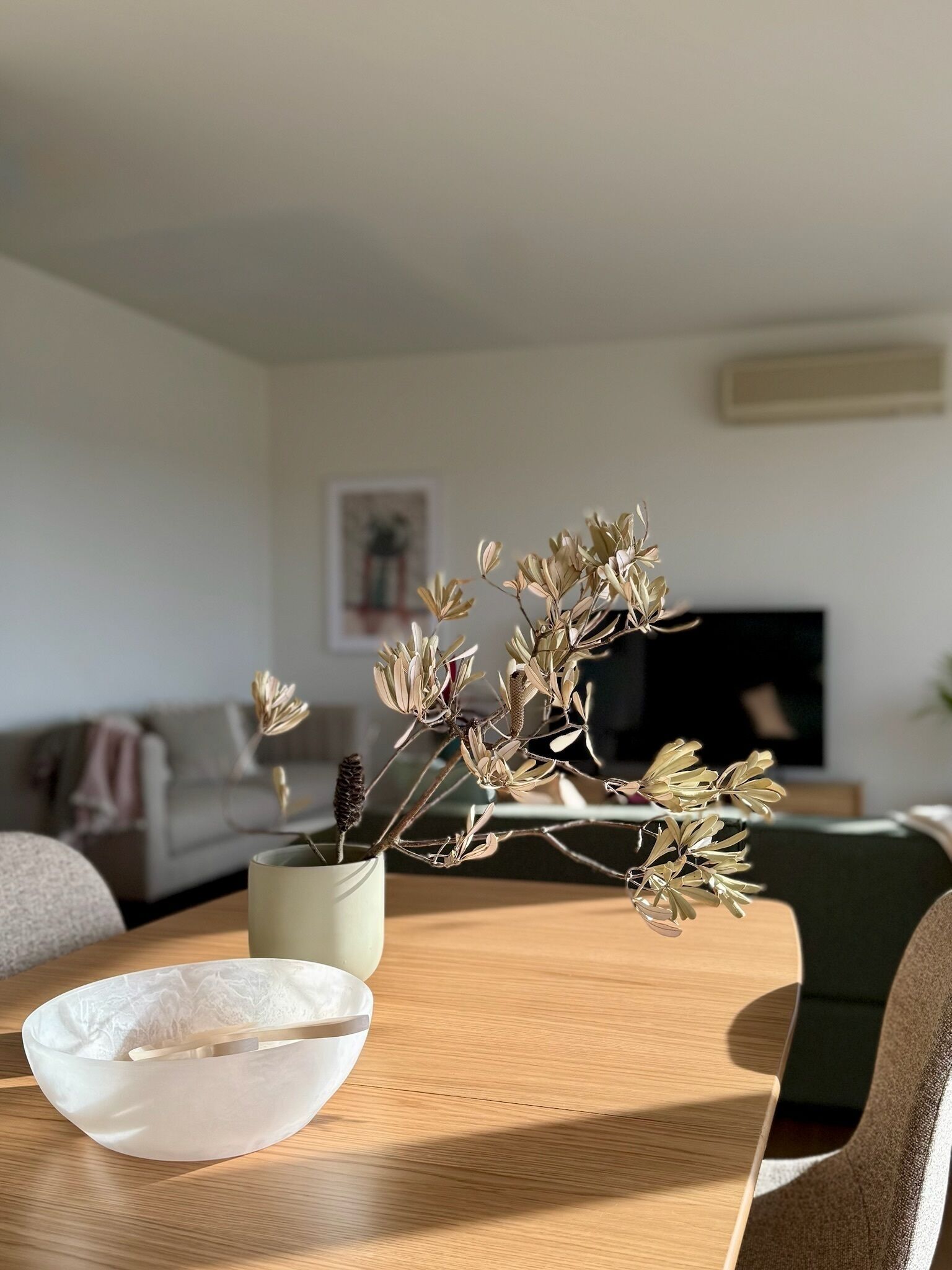 Una mesa de comedor con un jarrón de flores secas, un cuenco y un sofá al fondo.
