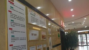 Un espace d’accueil avec plusieurs affiches informatives accrochées au mur, une plante en pot et une porte d’entrée en verre.