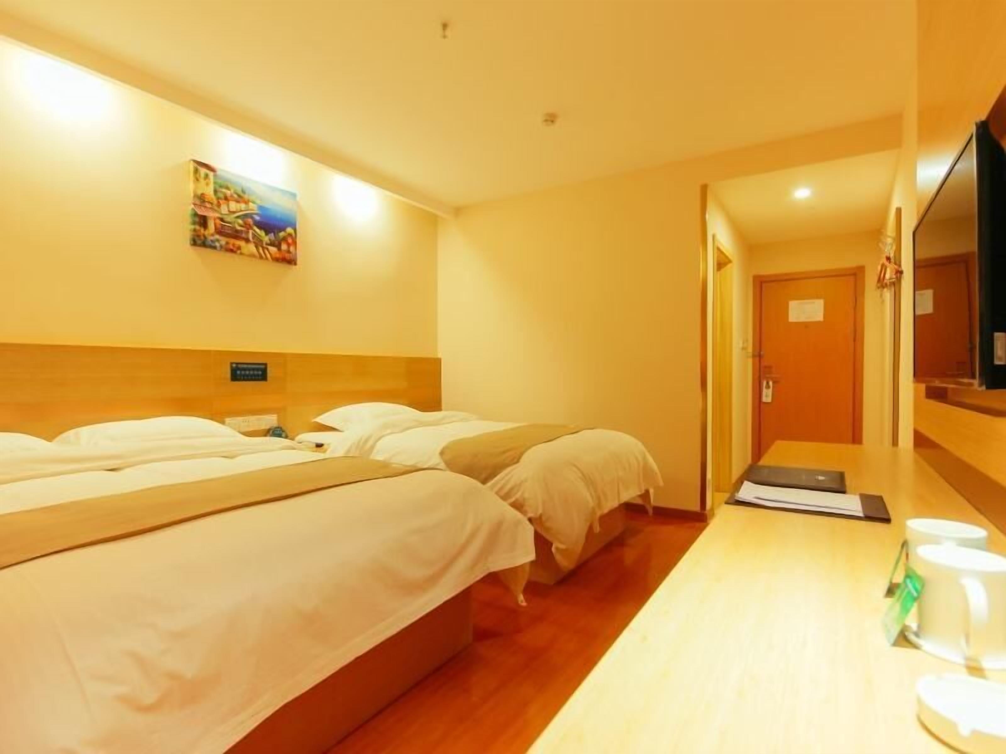 Une chambre d’hôtel avec deux lits, une tête de lit en bois, un téléviseur à écran plat et une petite table avec une tasse et une soucoupe.