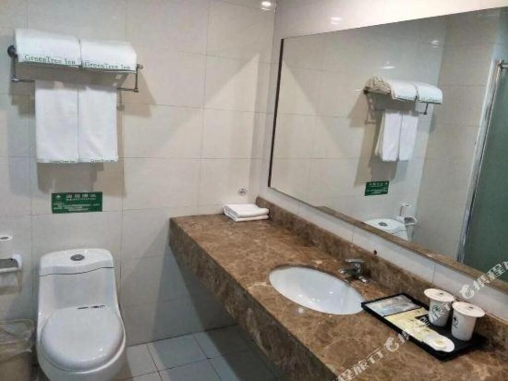 Een badkamer met toilet, wastafel en spiegel. Handdoeken hangen aan een rek en een bordje met het kamer nummer.
