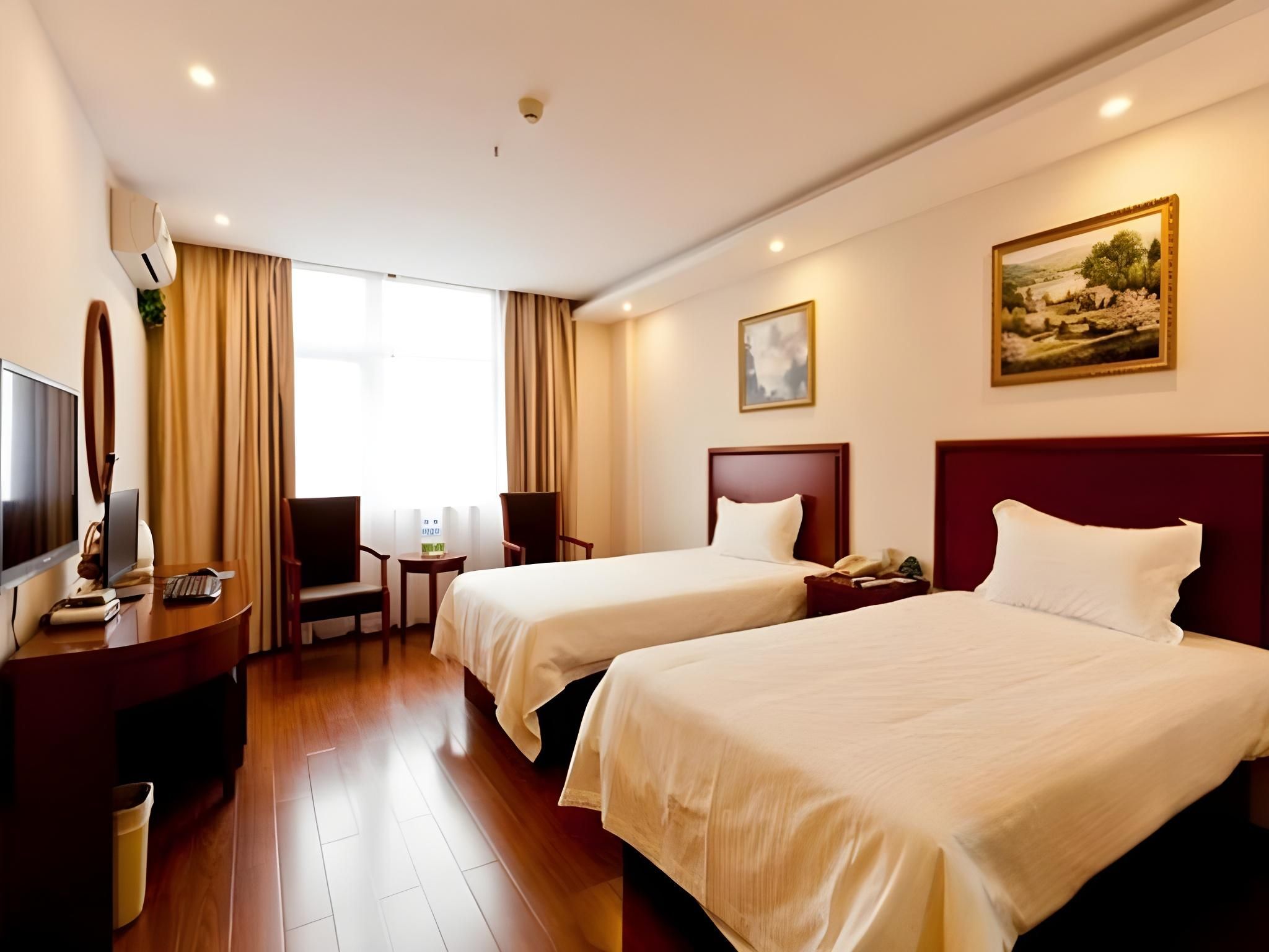 Une chambre d’hôtel avec deux lits, un bureau avec un ordinateur, une chaise, une télévision et un tableau au mur.