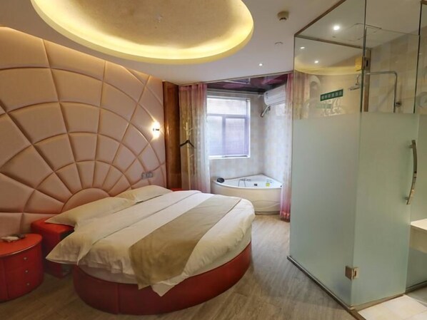 A modern bedroom with a large bed, a glass-enclosed shower, and a small red side table.