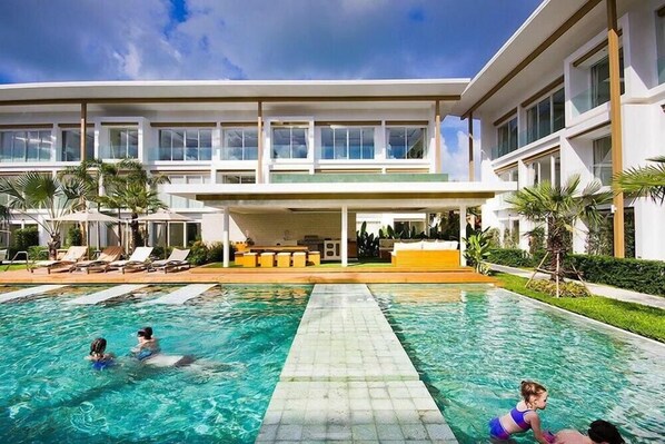 A modern hotel with a swimming pool, lounge chairs, and a covered seating area. - Chi Samui Resort (Koh Samui)