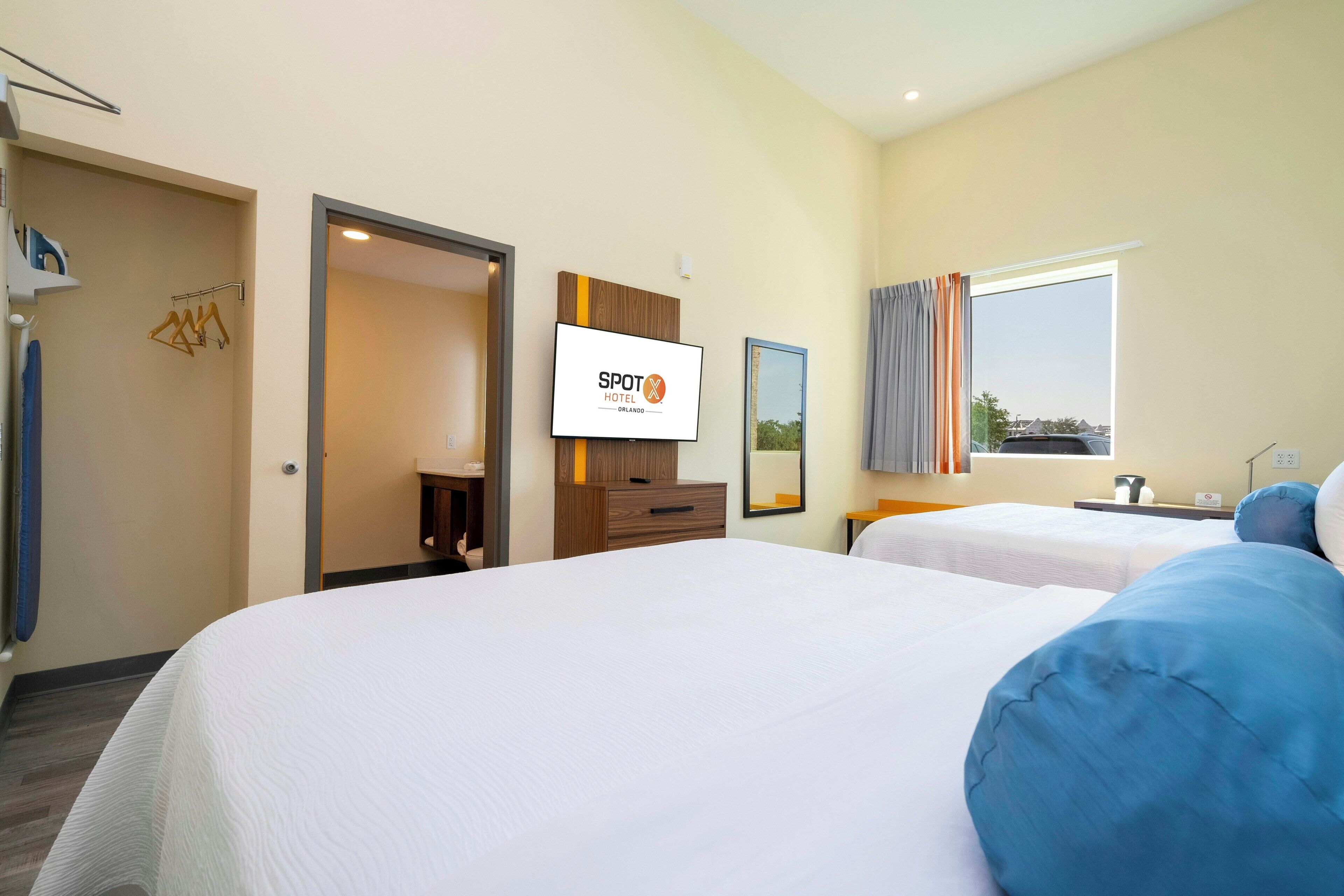 Ein Hotelzimmer mit zwei Betten, einem Fernseher, einem Kleiderschrank, einem Spiegel und einem fenster mit Vorhängen.