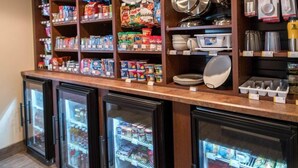 Uma área de cozinha com prateleiras repletas de alimentos, utensílios de cozinha e louças.