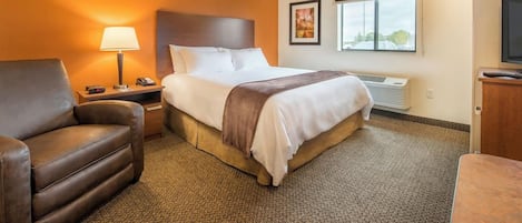 A hotel room with a bed, a chair, a lamp, a TV, and a window.