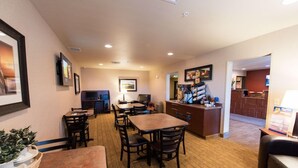 A hotel lobby with a reception desk, several tables and chairs, a television, and framed pictures on the walls. - My Place Hotel-pittsburgh North/monaca, PA (Monaca)