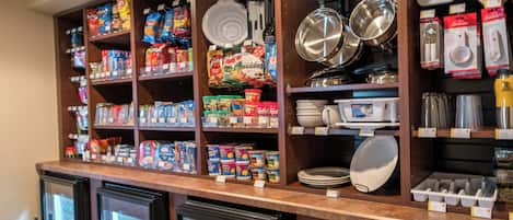Un espace cuisine doté d’étagères remplies de produits alimentaires, d’ustensiles de cuisine et de vaisselle.