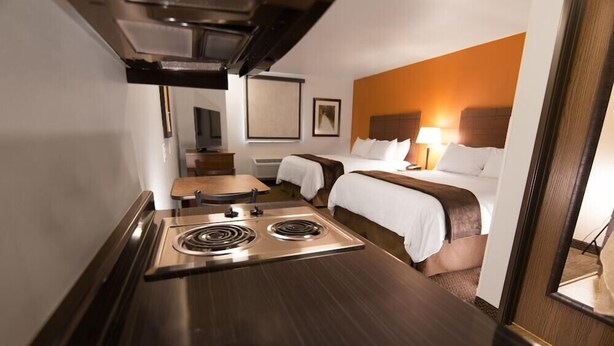 Quarto de hotel com cozinha compacta, duas camas, um espelho grande e vista para o corredor.
