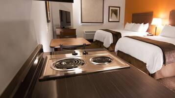 A hotel room with a kitchenette, a bed, a bedside table, and a chair.