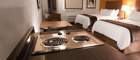 A hotel room with a kitchenette, a bed, a bedside table, and a chair.