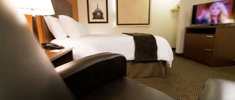 Een hotelkamer met een bed, een bureau met een lamp, een televisie en een bruine leren fauteuil.
