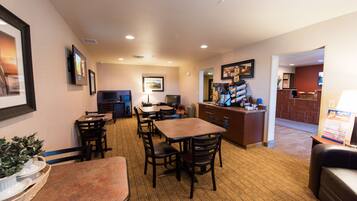 A hotel dining area with tables and chairs, a coffee station, and a television mounted on the wall.
