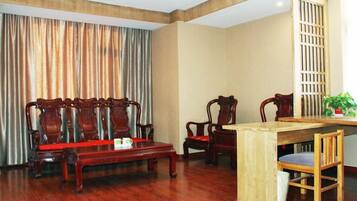 A room with a wooden dining table, four wooden chairs, a sofa, and a curtain.