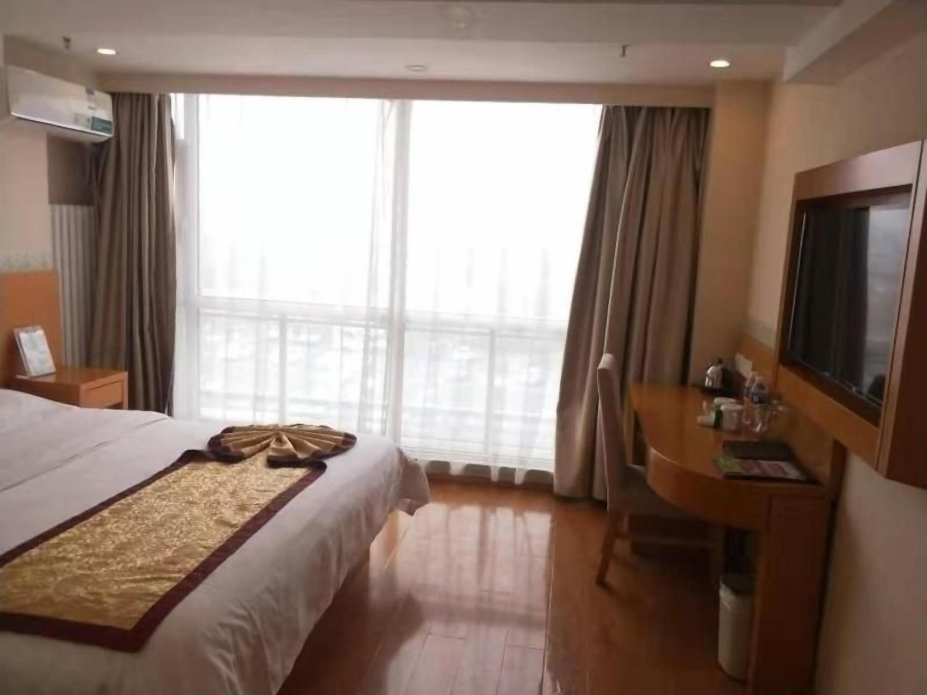 Een hotelkamer met een groot bed, een bureau, een stoel, een televisie en een raam met gordijnen.