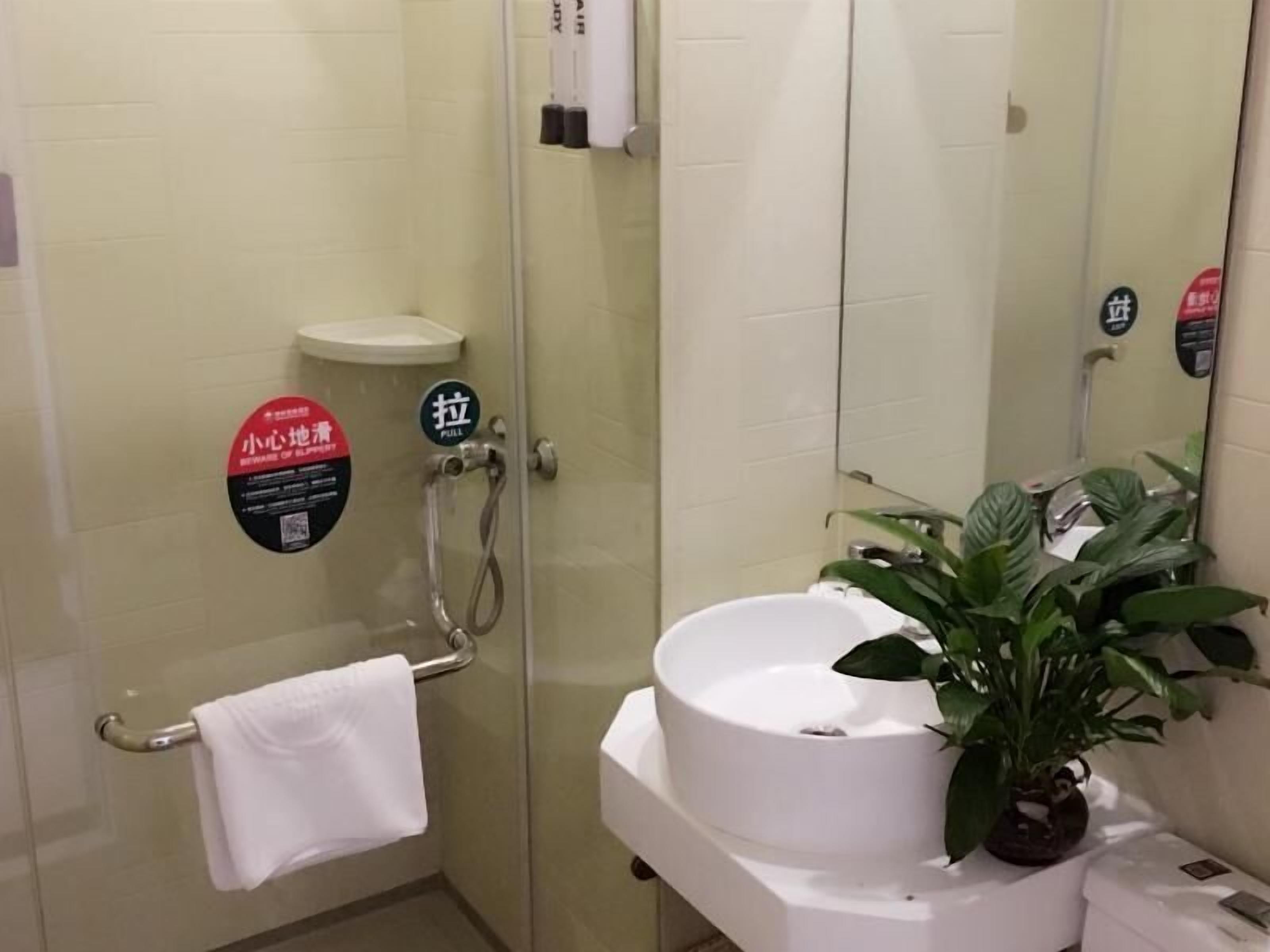 A bathroom with a glass shower enclosure, a white sink, a towel rack, and a potted plant.