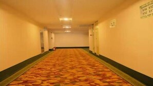 A long, narrow hotel corridor with a patterned carpet, walls with contact numbers, and doors on both sides.
