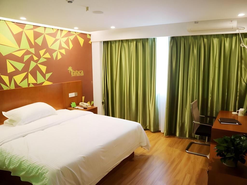 A hotel room with a large bed, a desk, a chair, and a green curtain.