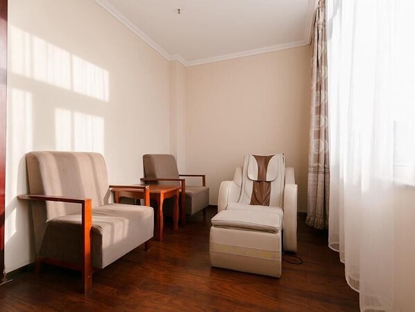A room with a wooden floor, a sofa, a chair, a massage chair, and a small table. - Greentree Inn Tangshan Caofeidian Free Trade Zone Municipal Building Express Hotel (Tangshan)