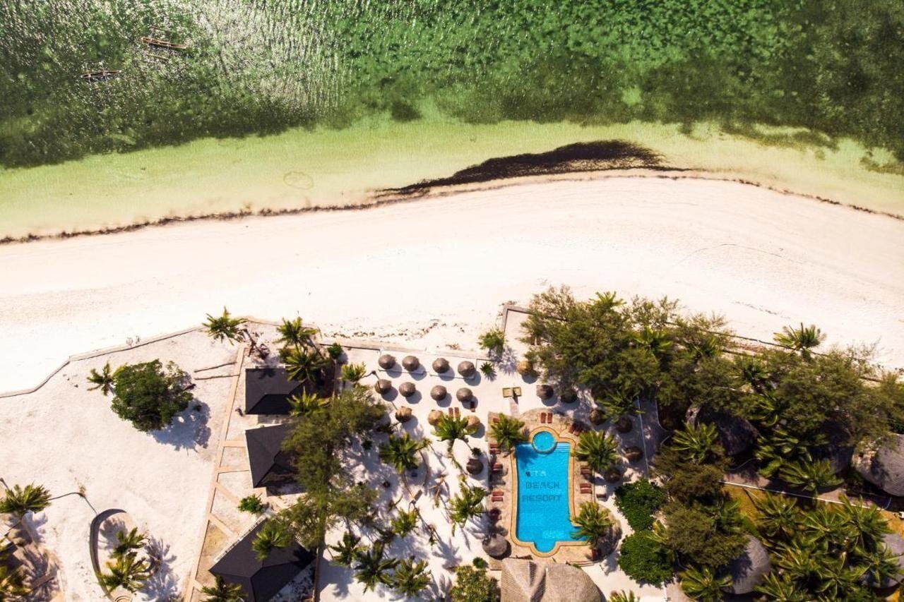 Vista aérea de um resort à beira-mar, com piscina, palmeiras e uma praia de areia.
