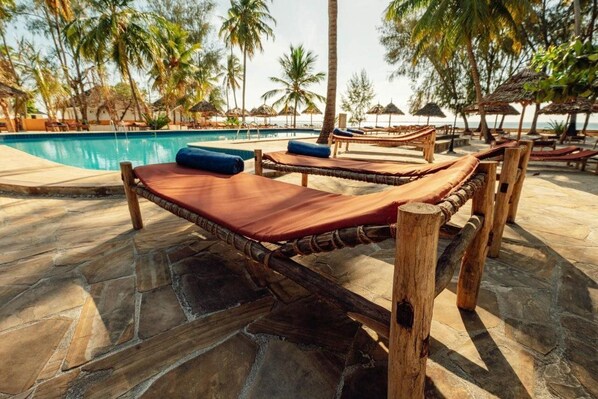 A poolside area with wooden loungers and a stone-tiled floor. - Sansi Kae Beach Resort (Michamvi)