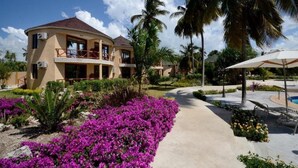 A resort with a curved building, a pool area with lounge chairs, and a garden with purple flowers. - Sansi Kae Beach Resort (Michamvi)